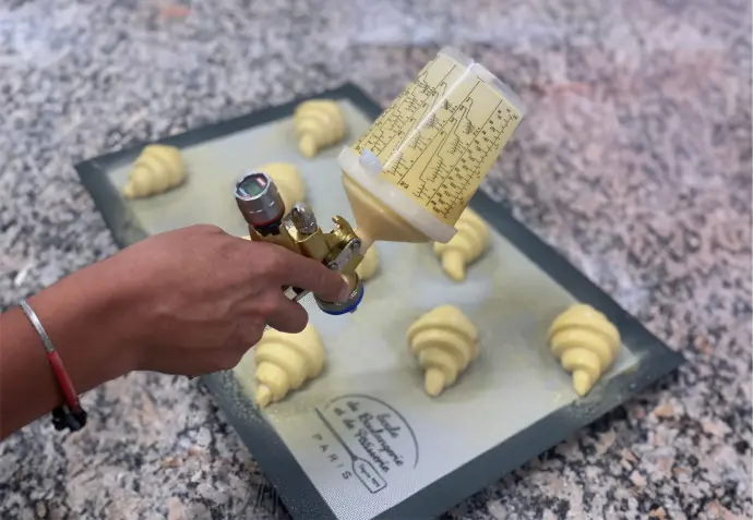 SATAjet1000 B RP Pastry edition avec godet RPS Pistolet SATAjet 1000 B RP Pastry Edition pulvérisant sur des croissants avec godet RPS